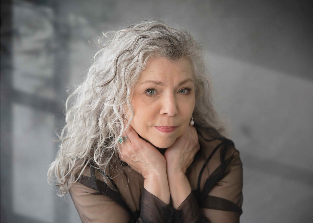 Ritratto autentico di donna over 50 con capelli grigi e rughe visibili, posa naturale, espressione forte e consapevole